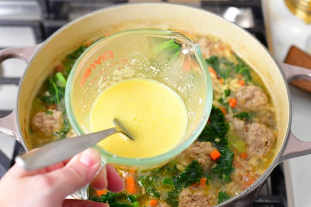 holding a cut with whisked egg over the pot of soup