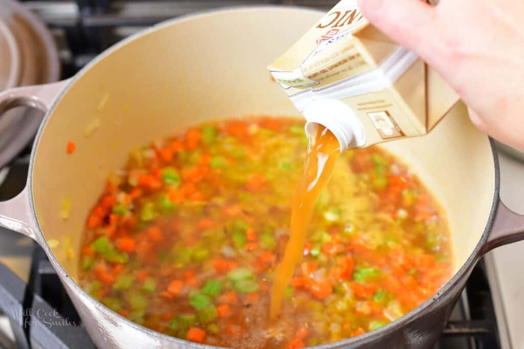 adding chicken stock to the pot with veggies