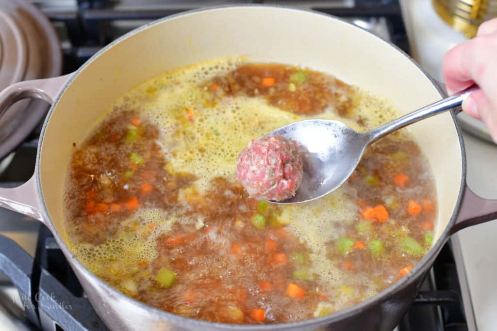 adding meatballs to the soup in the pot