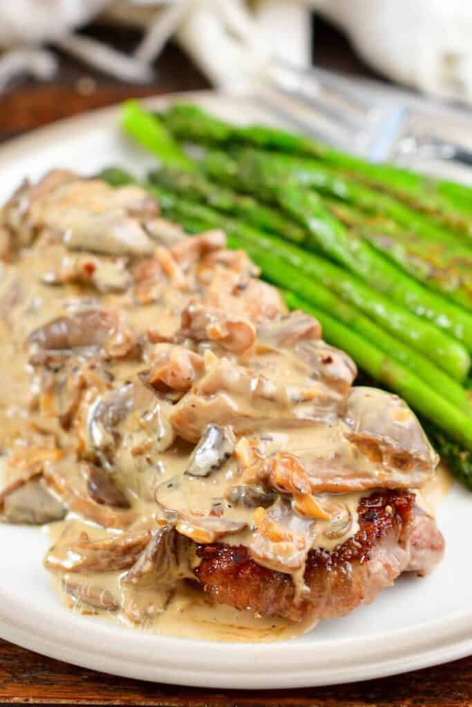 closeup of steak topped with mushroom sauce ad some asparagus