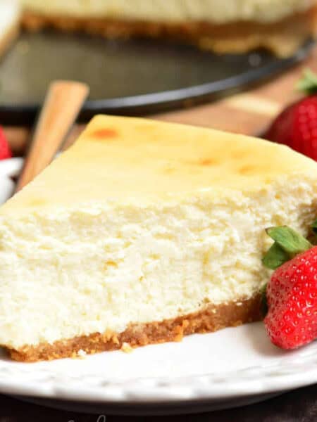 a slice of NY style cheesecake on the plate with strawberries around.