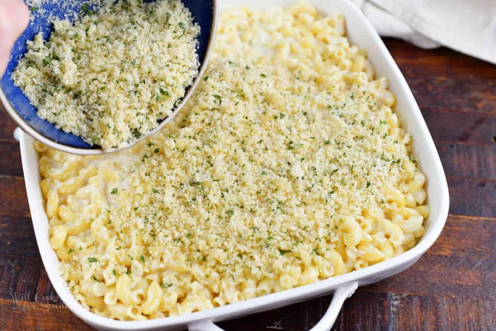 adding the parmesan topping to mac and cheese in a dish