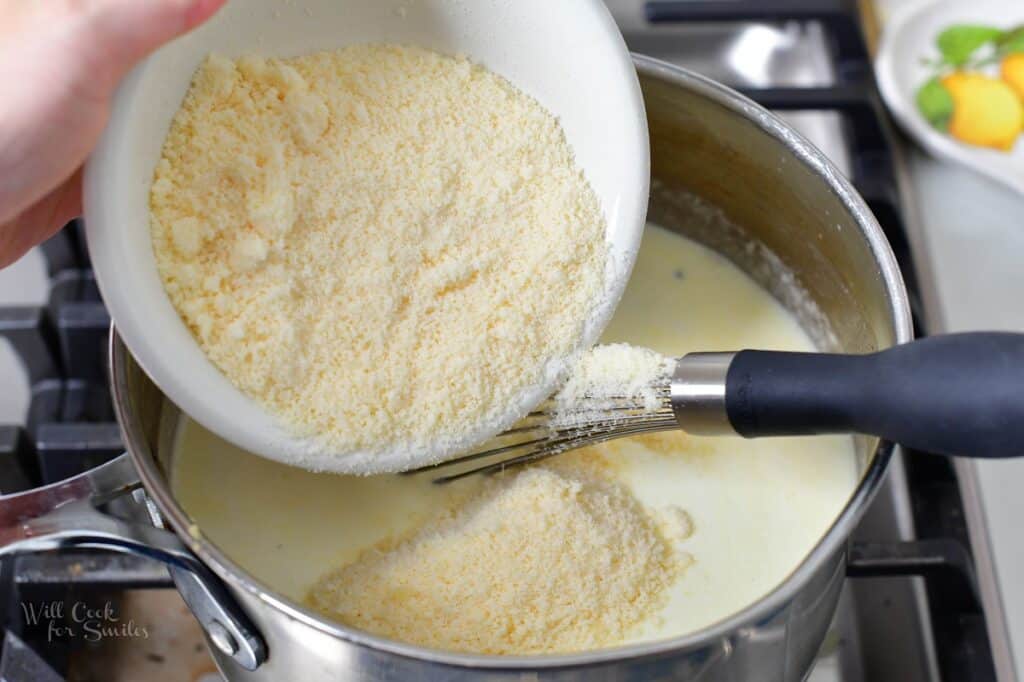 adding grated parmesan cheese to the pot with cheese sauce