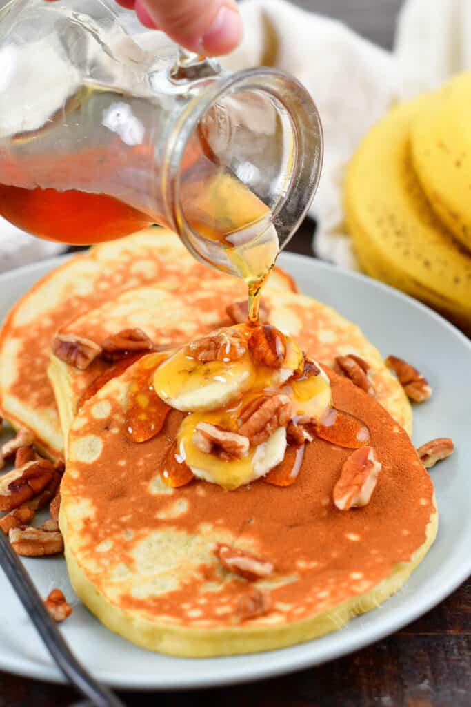 pouring maple syrup over banana pancakes