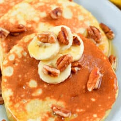 closeup of banana pancakes on a plate with nuts and syrup