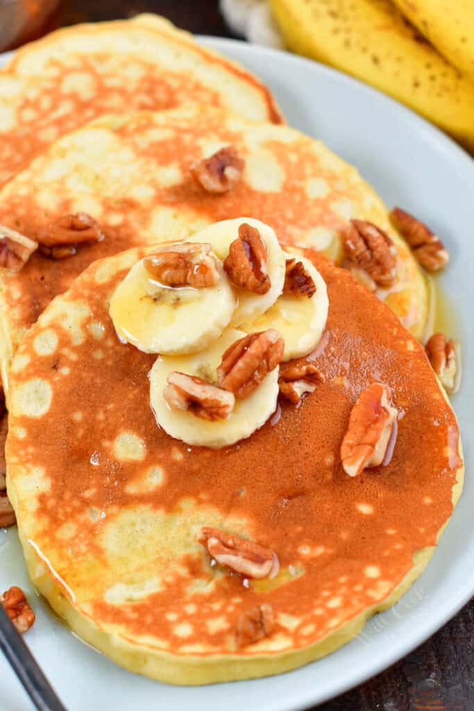 closeup of banana pancakes on a plate with nuts and syrup