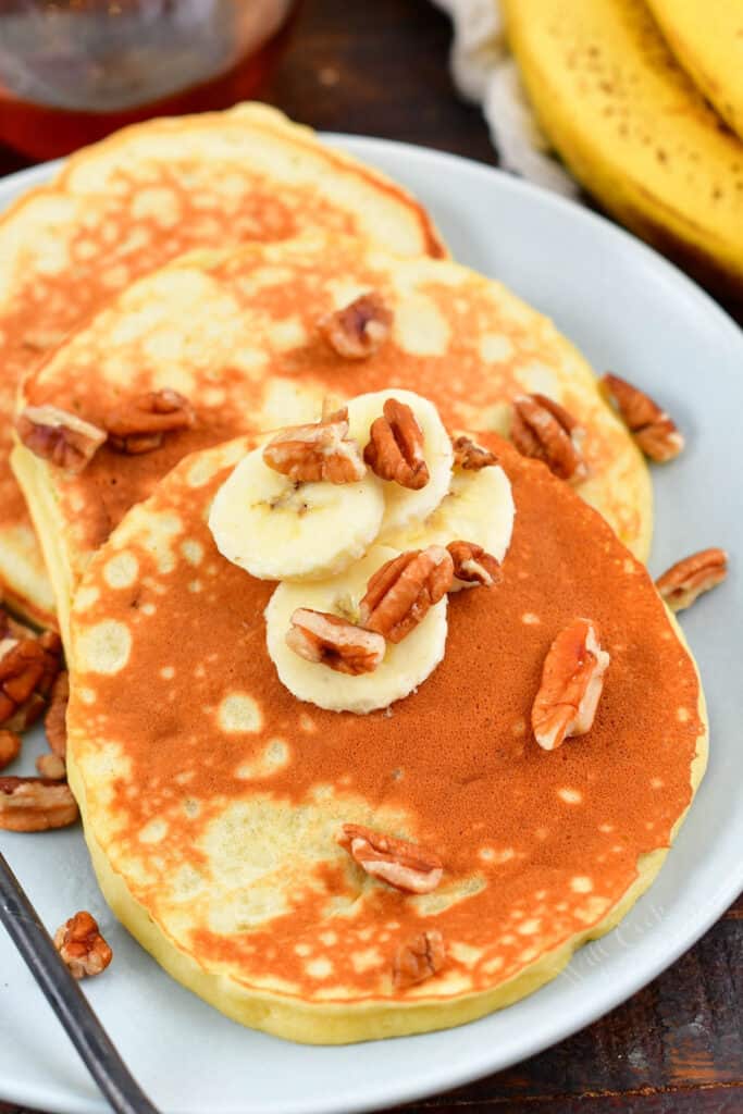 stack of three pancakes on a plate topped with bananas and nuts