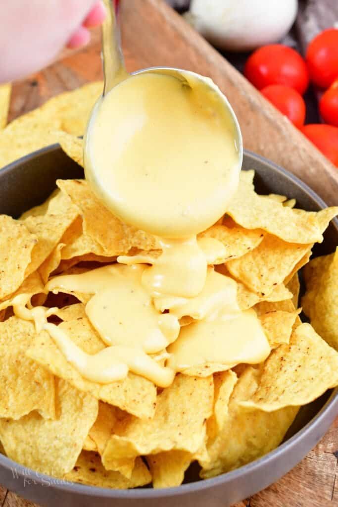 adding nacho cheese to the chips in a bowl