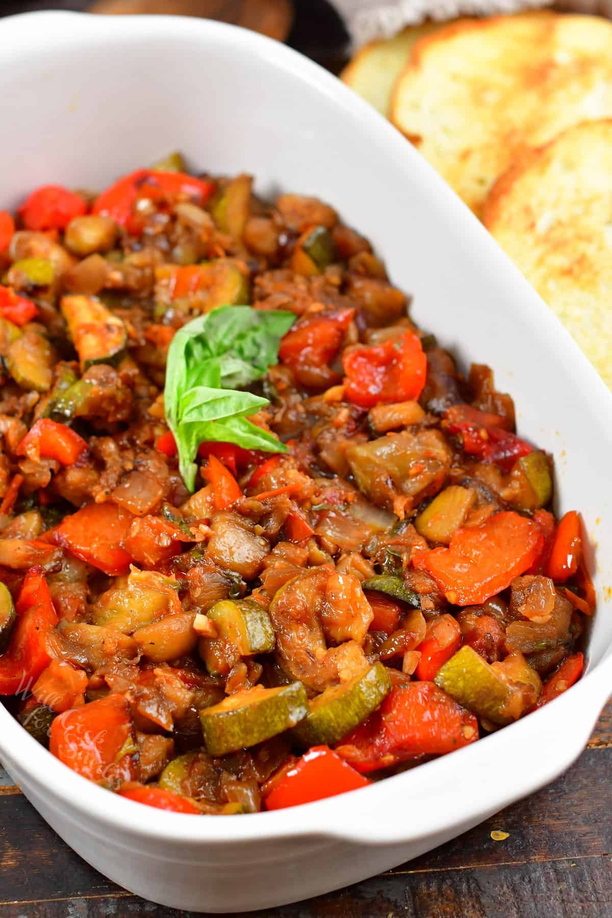 ratatouille in a white dish with basil and bread