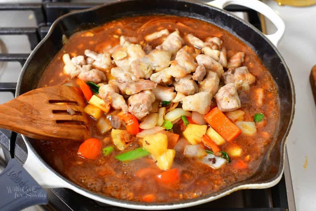 adding vegetables and chicken to the sauce in the pan