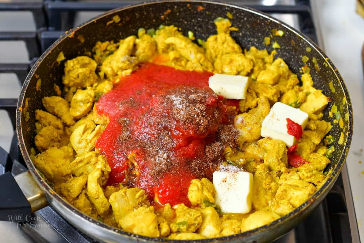 adding tomato sauce, spices, and butter to chicken cooking in a bowl