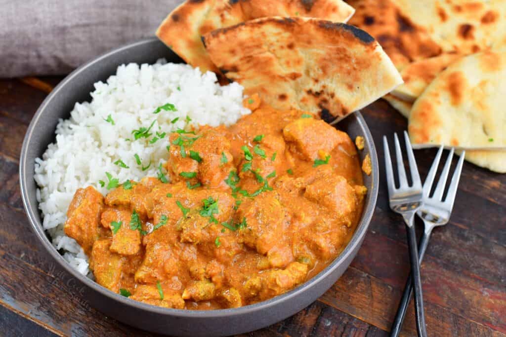 butter chicken in a bowl with naan and rice