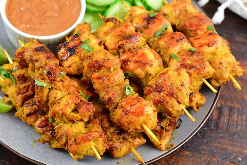 side look of chicken satay skewers on a plate with sauce