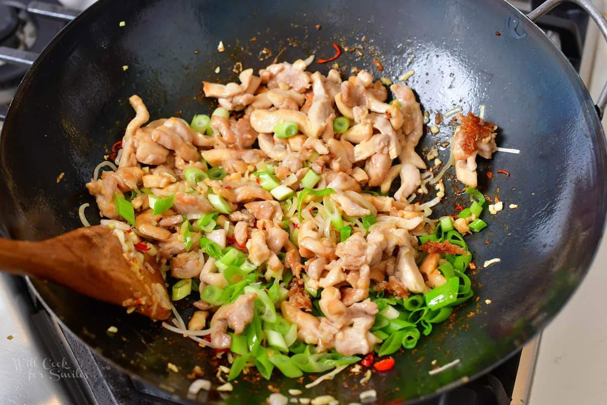 mixing greens and chicken in a wok