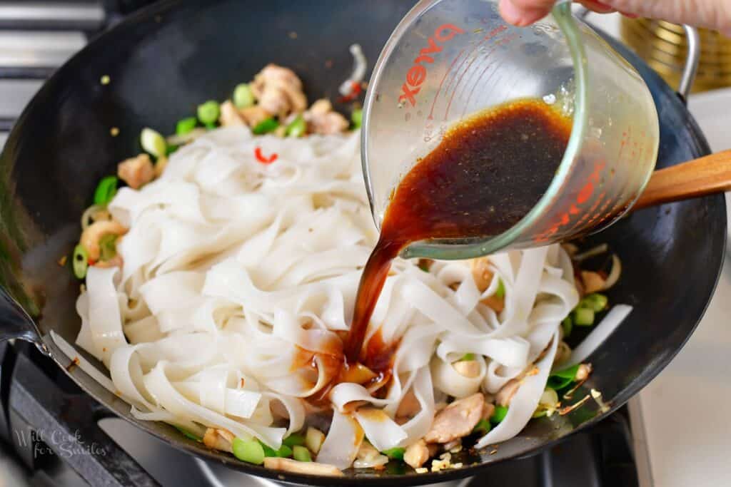 adding sauce to the noodles in a wok