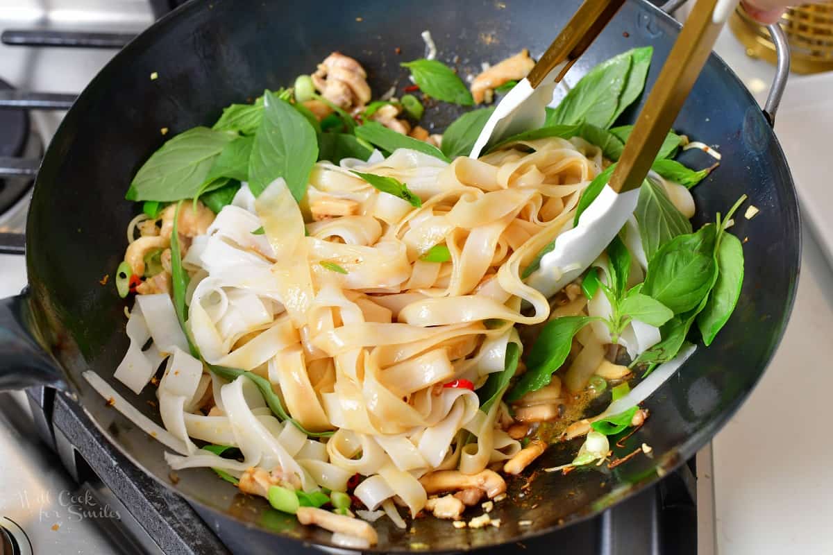 tossing noodles and basil with sauce in a wok