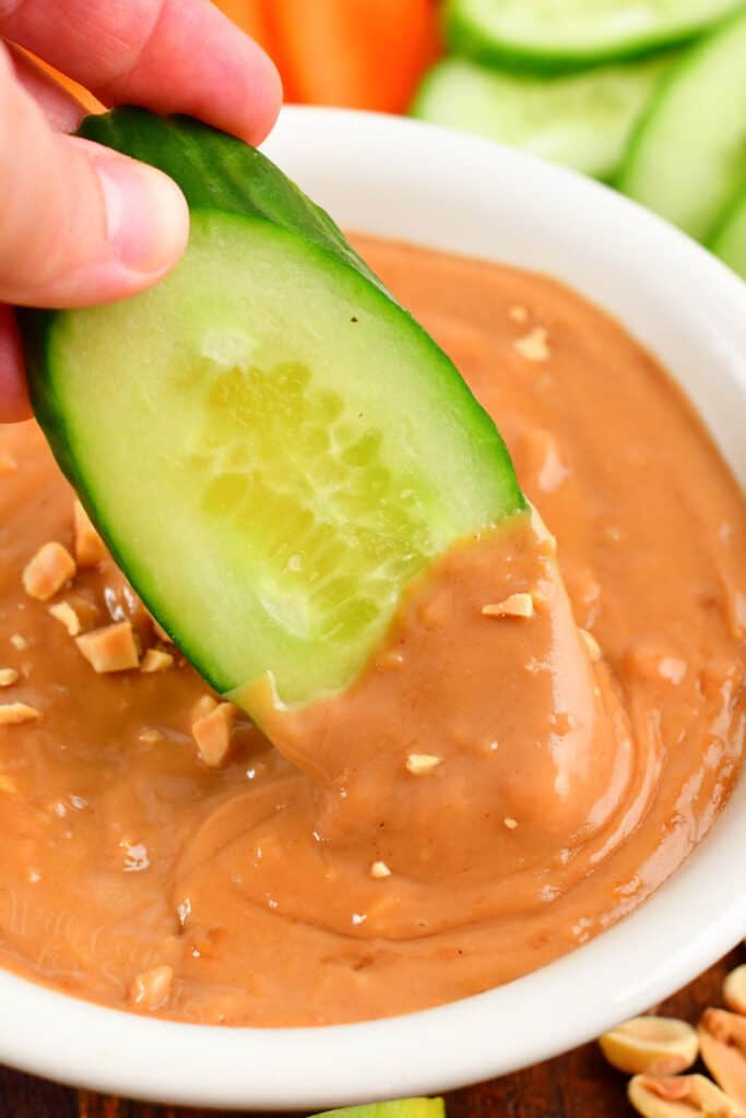 closeup of dipping a cucumber into peanut sauce