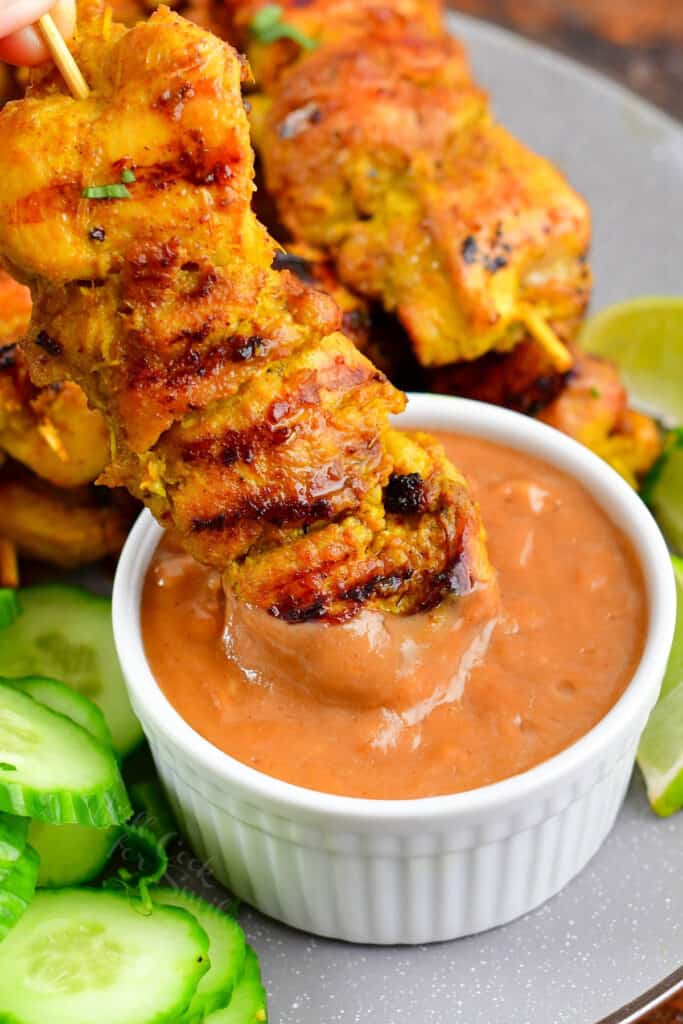 dipping chicken satay into peanut sauce