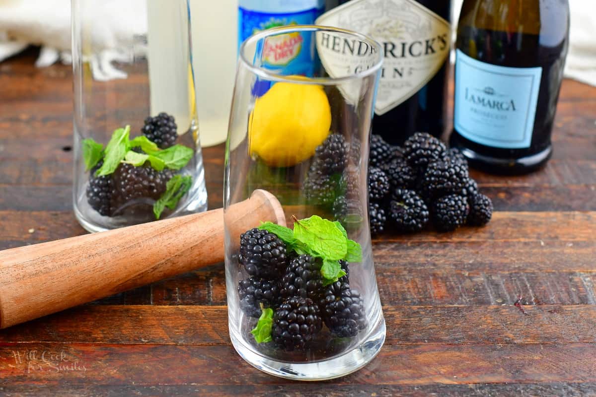 blackberries and mint in the glass next to muddler