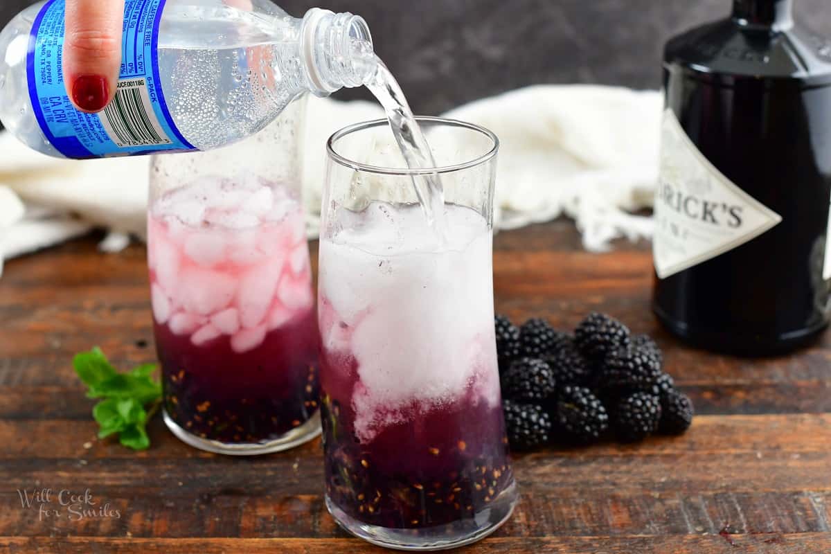pouring in club soda into the glass with blackberries