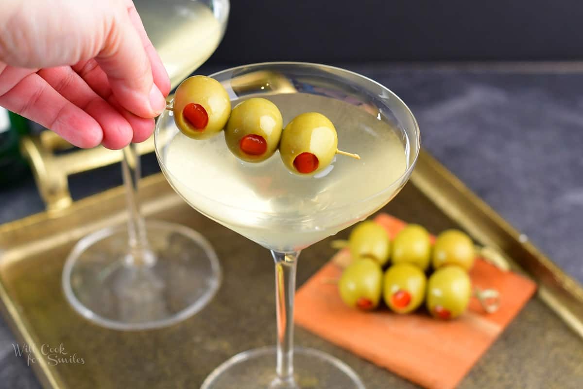 adding olives to the martini in a glass