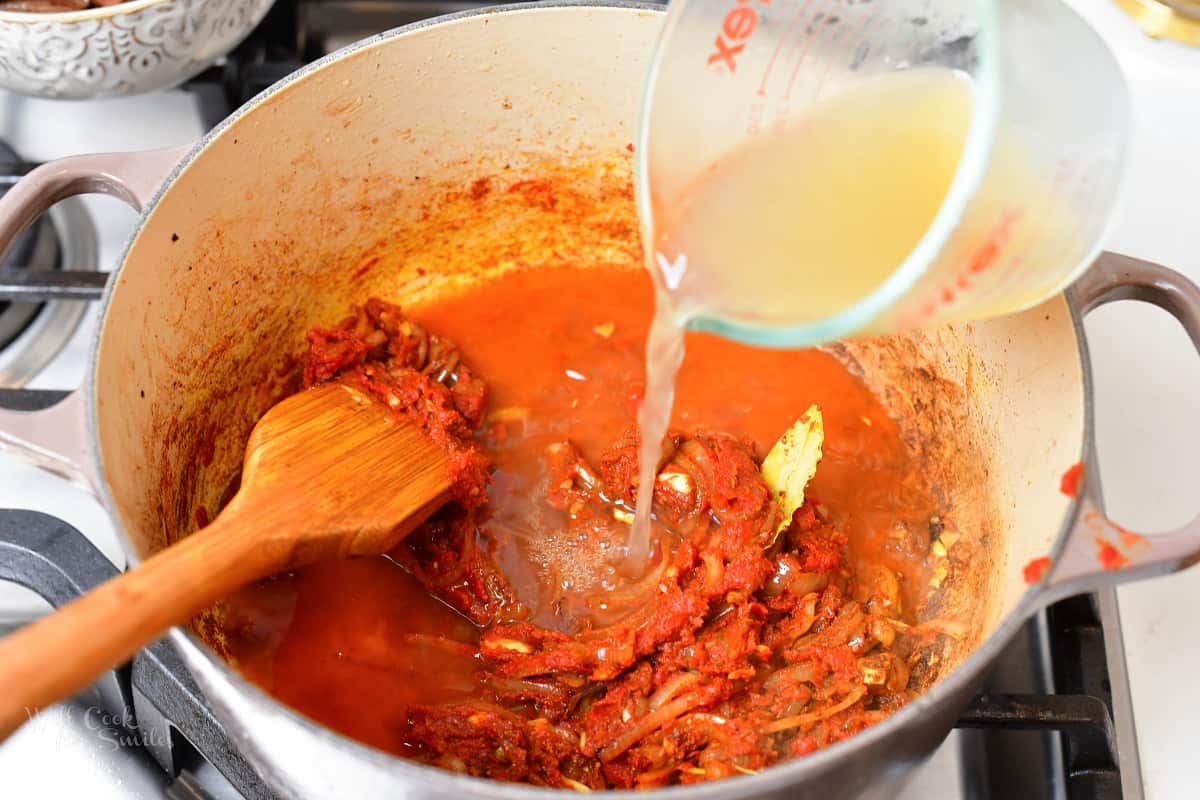 adding broth into the pot with tomato sauce and spices
