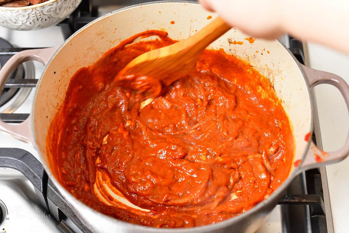 stirring tomato sauce into the pot with onions and spices