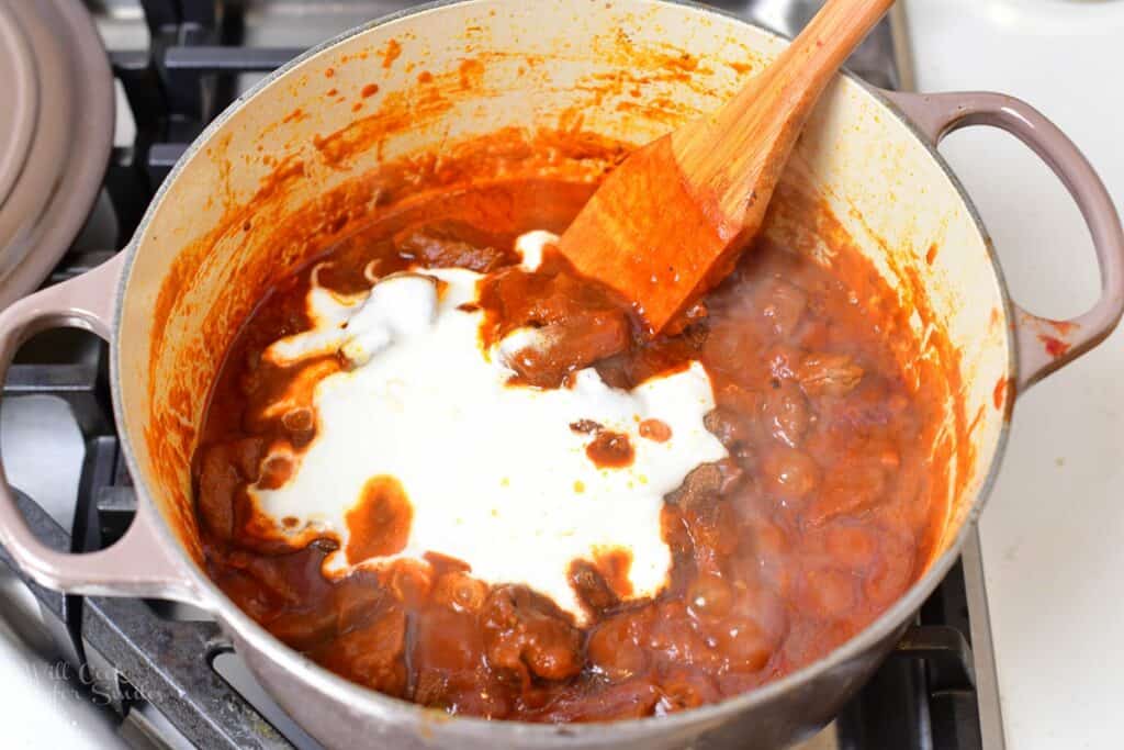 adding Greek yogurt to the stewing lamb in the pot