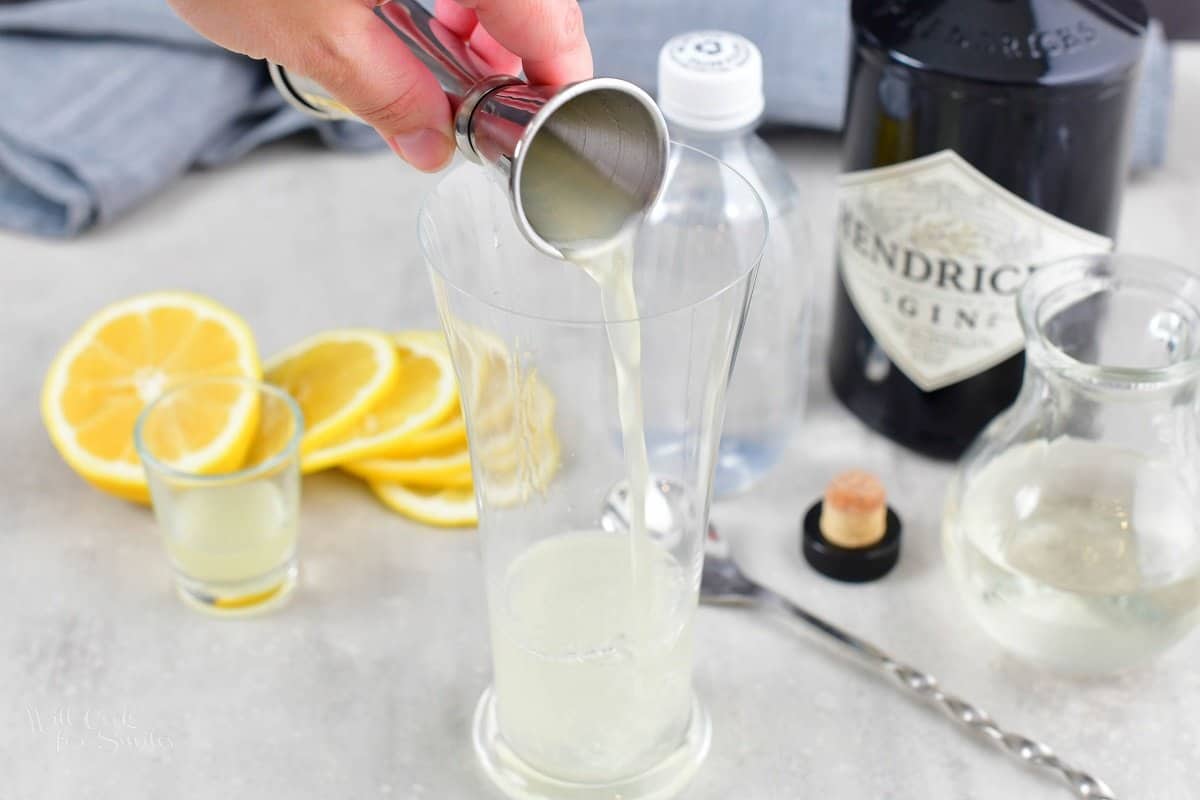 adding lemon juice to the tall glass with gin