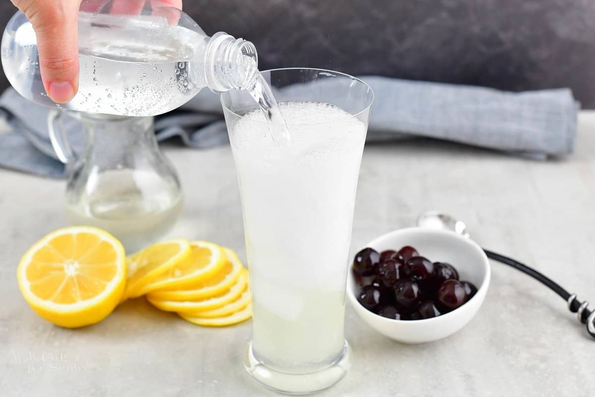 adding club soda to the cocktail with lemons and cherries around