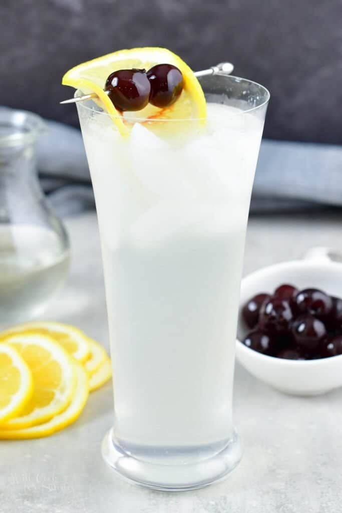 Tall image of the light yellow cocktail with lemon and cherries
