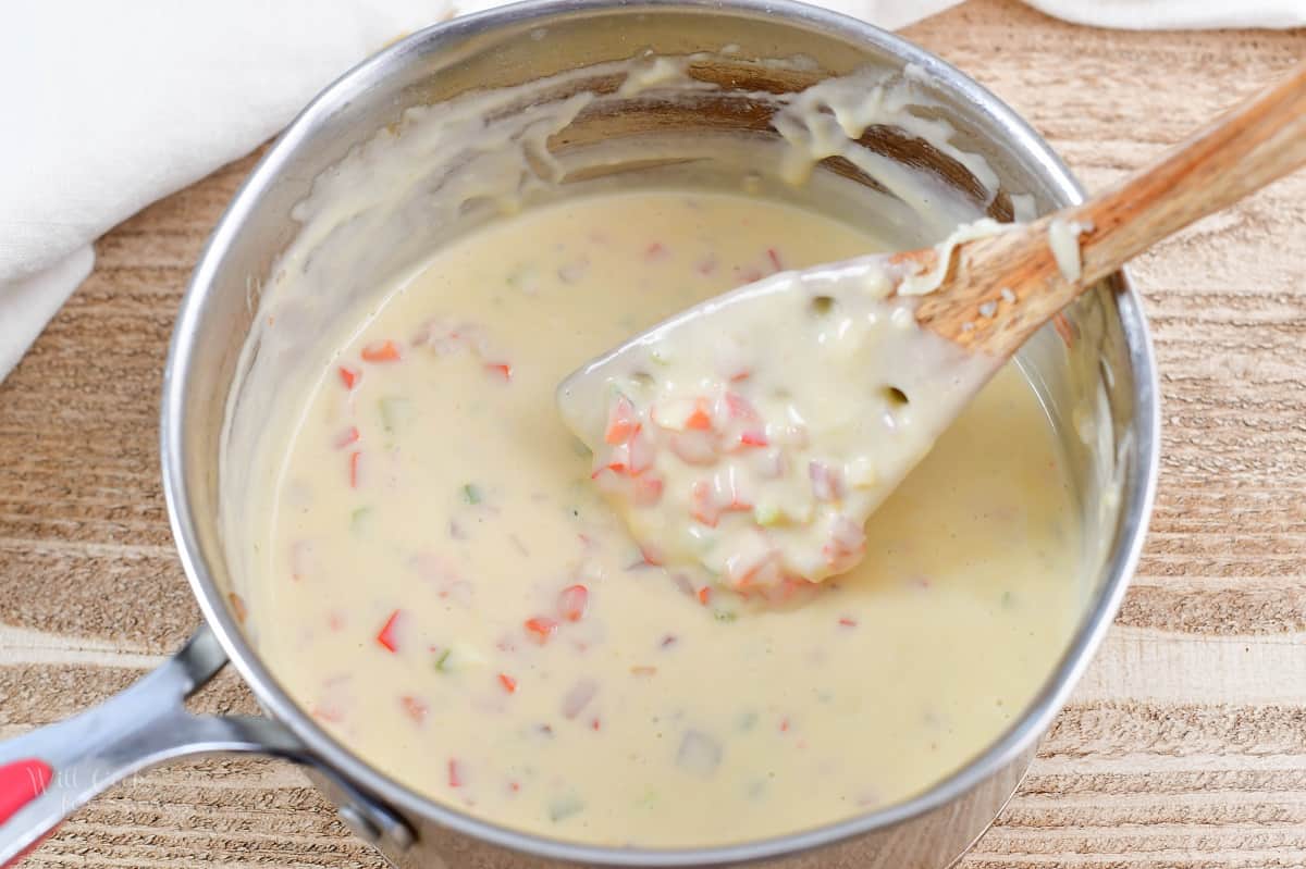 stirring queso dip in a pot with a wooden spoon