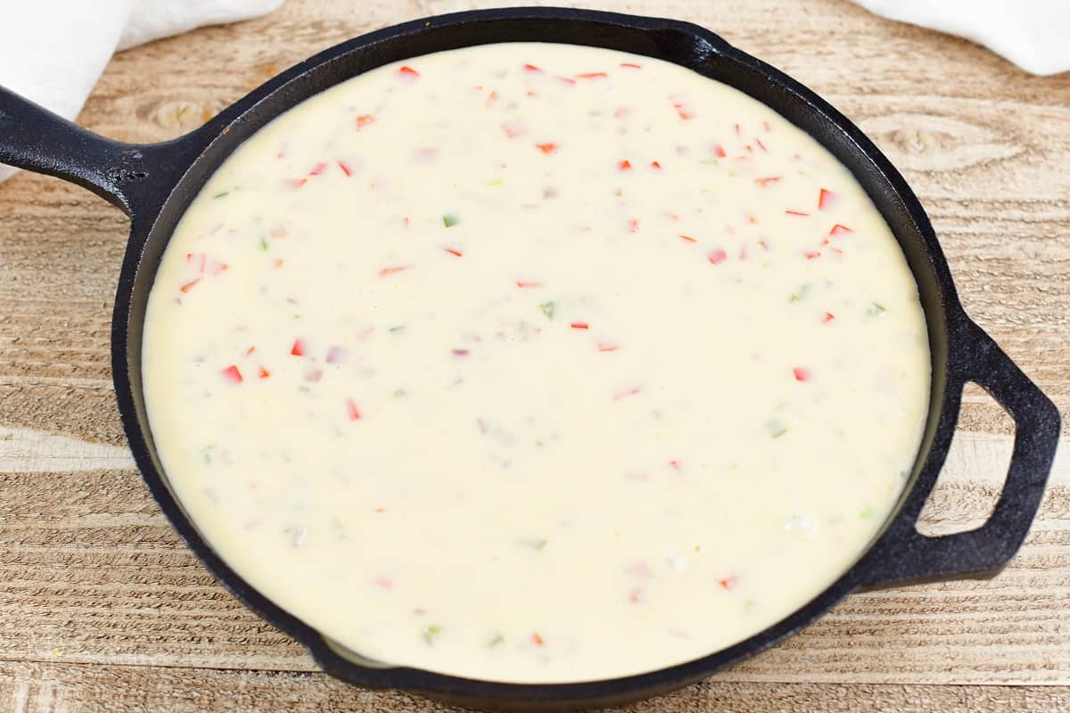 queso poured over refried bean mixture in a skillet