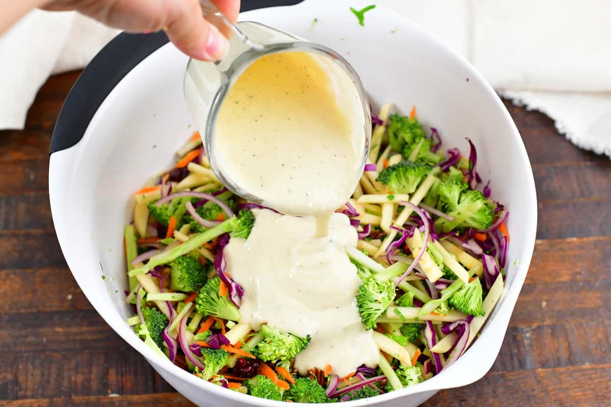 adding slaw dressing to the bowl with sliced veggies