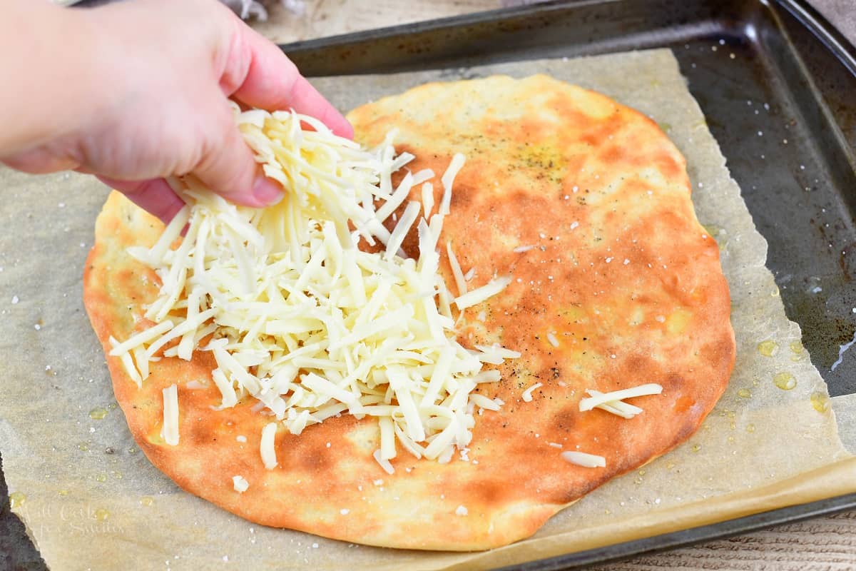 spreading shredded cheese on the pre-baked pizza dough