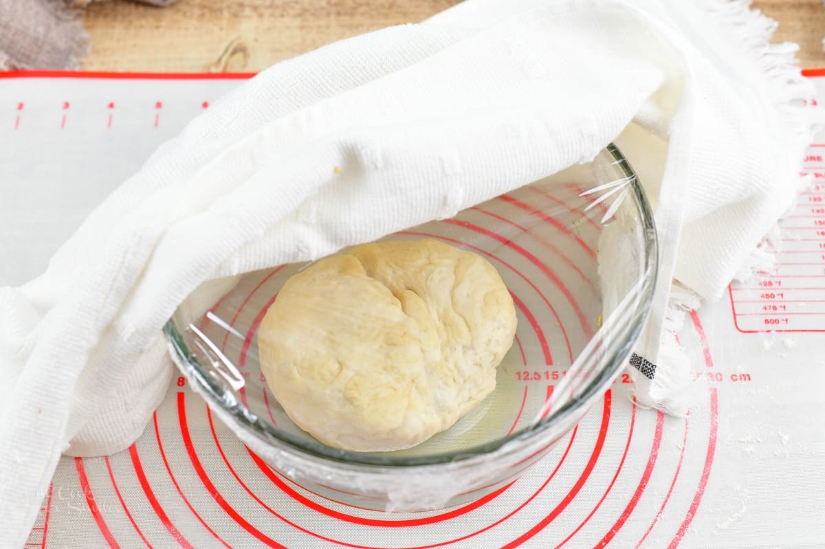 dough in the glass bowl covered in plastic wrap and towel
