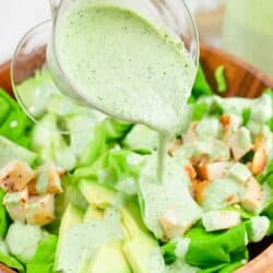 pouring the green goddess dressing over the salad in a bowl