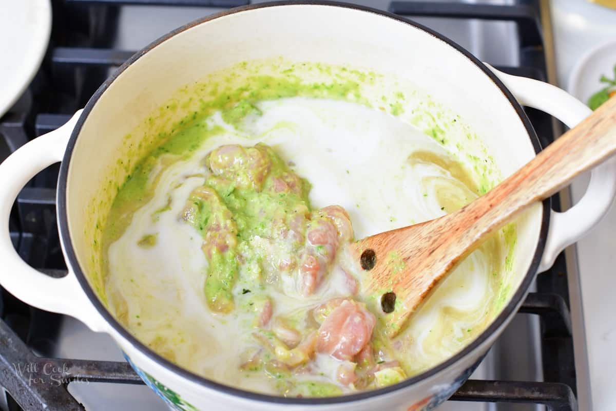 stirring chicken into the green curry and coconut milk in a bowl