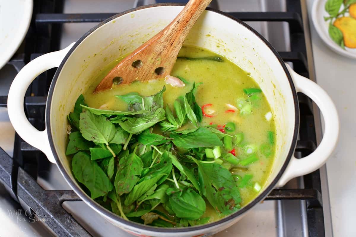 adding Thai basil to the green curry in a bowl