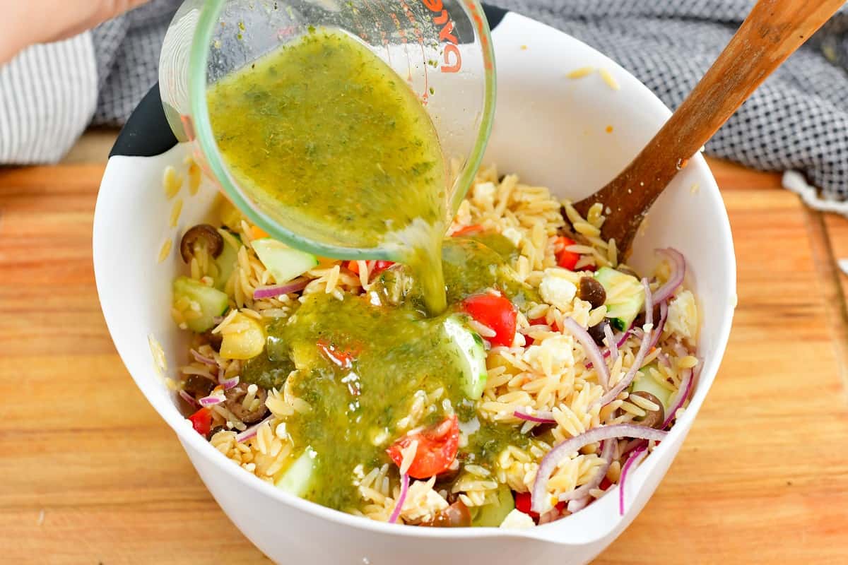 pouring in Greek dressing into orzo salad