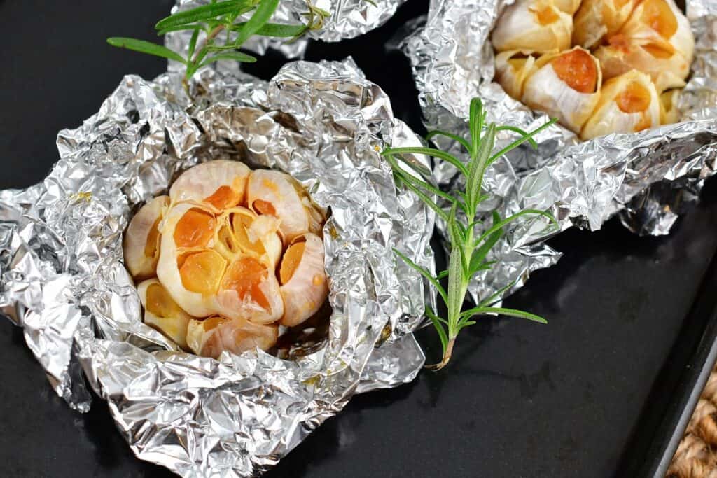 roasted garlic cloves in foil on baking sheet with rosemary