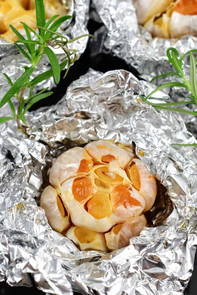 closeup of roasted garlic in foil with rosemary