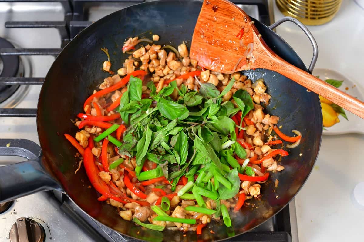 adding Thai basil to the cooked chicken in a wok