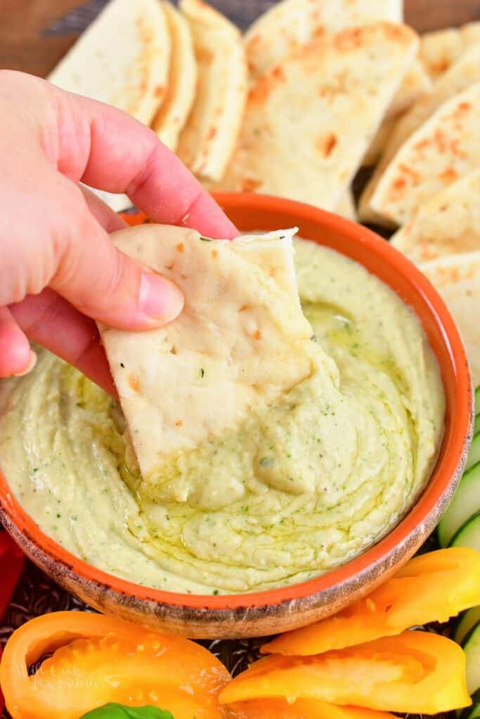 dipping pita bread into white bean dip