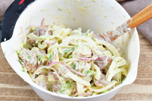 mixing potato salad in a white mixing bowl