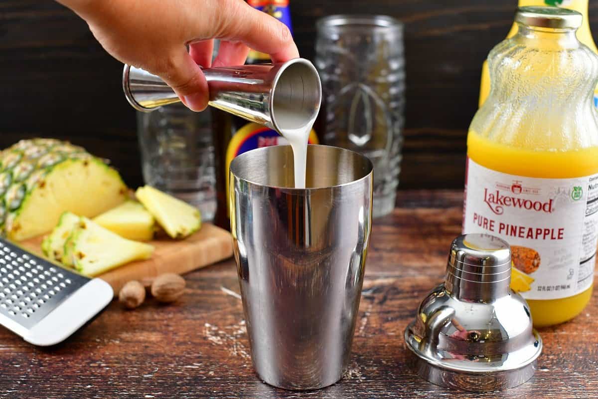 adding cream of coconut to the cocktail shaker