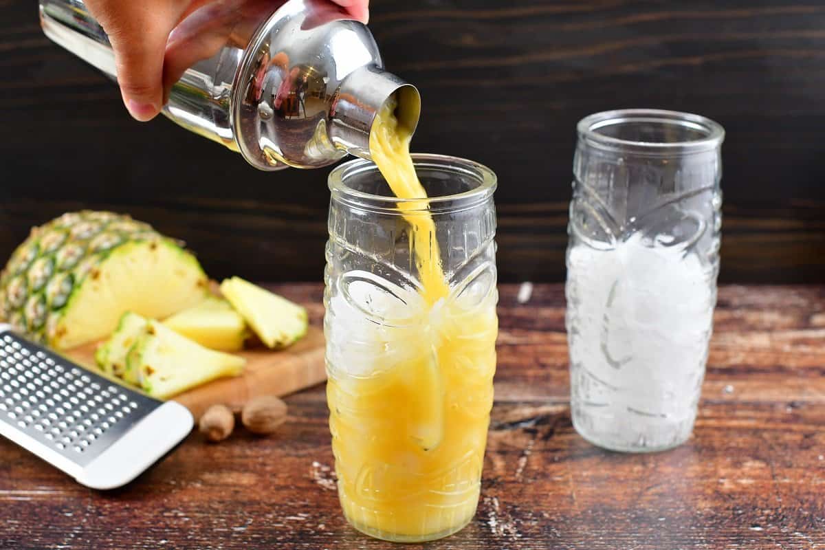 pouring the shaken yellow cocktail into the tiki glass