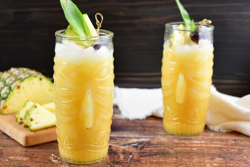 two glasses with yellow painkiller cocktail and sliced pineapple