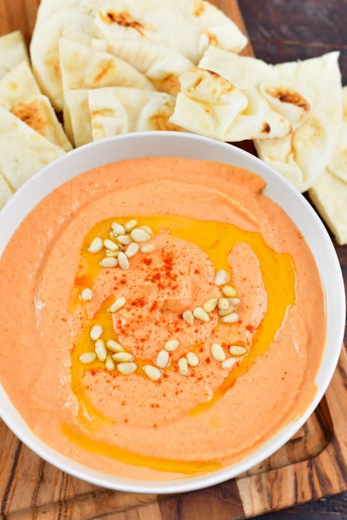 top view of bell pepper hummus with pine nuts and na'an