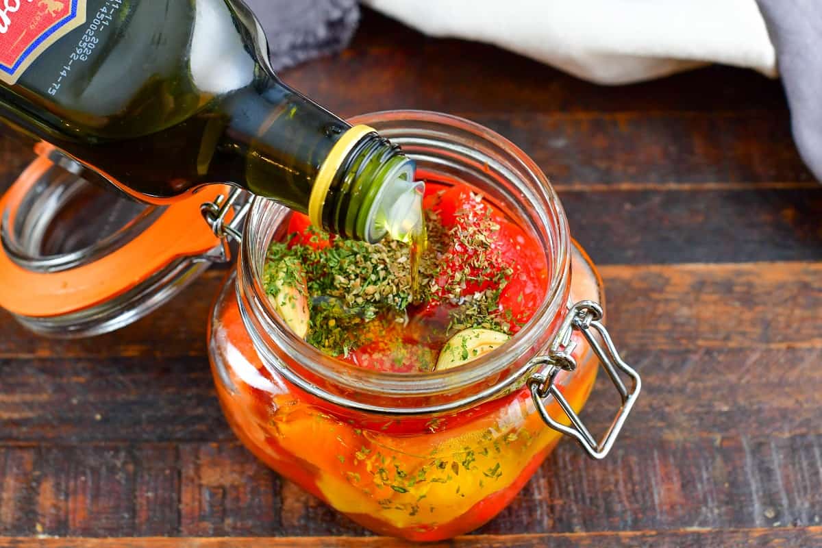 adding oil to roasted peppers in a jar with herbs